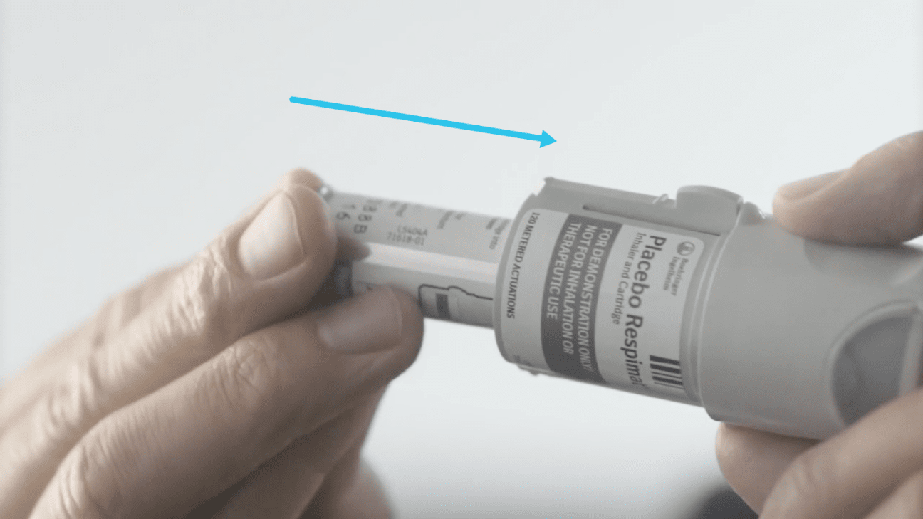 Hands inserting a medication cartridge into the base of a Respimat inhaler.