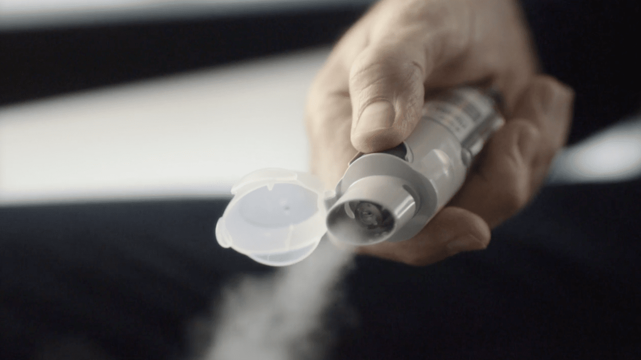 Hand pressing the dose-release button on a Respimat inhaler, releasing a visible mist
