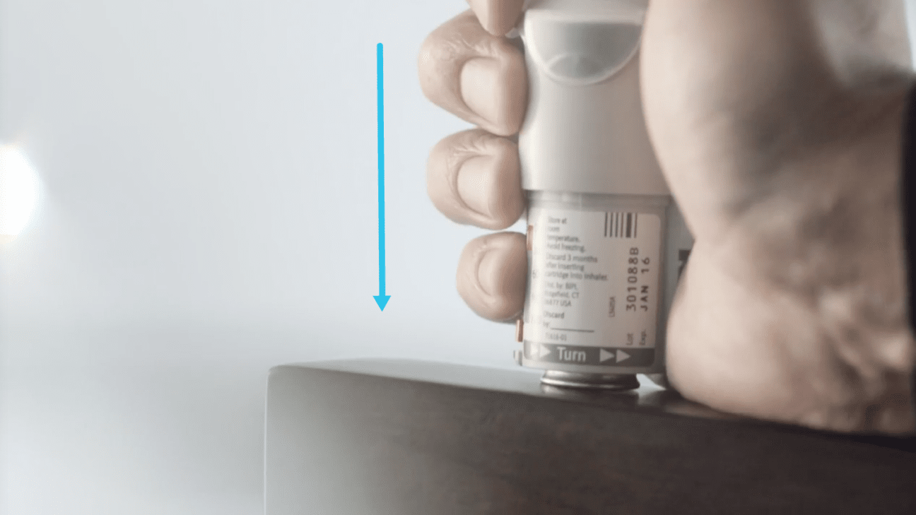 Hand pushing a Respimat inhaler down against a firm surface to secure the cartridge.