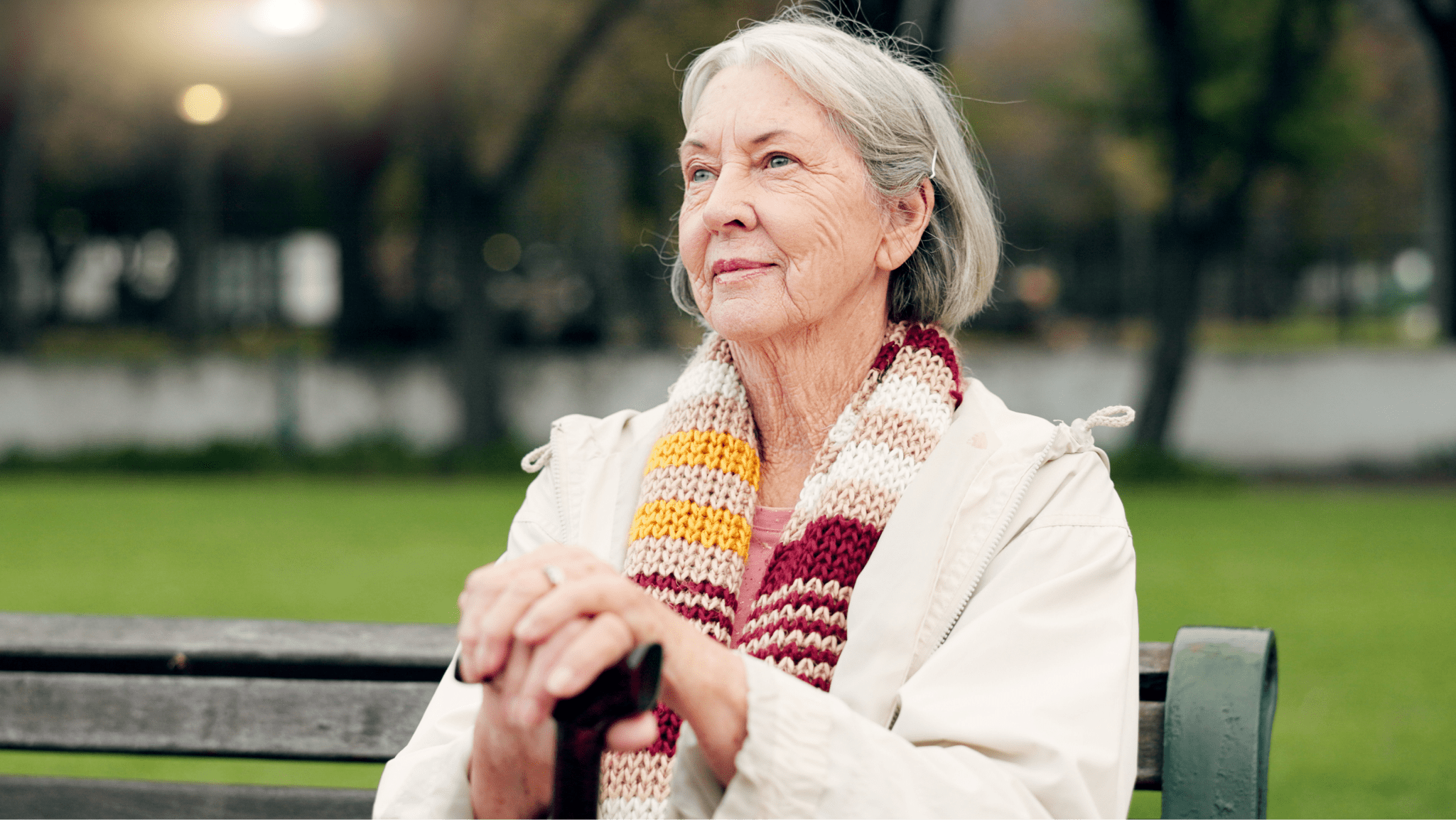 Senior woman with a cane sitting on a park bench.